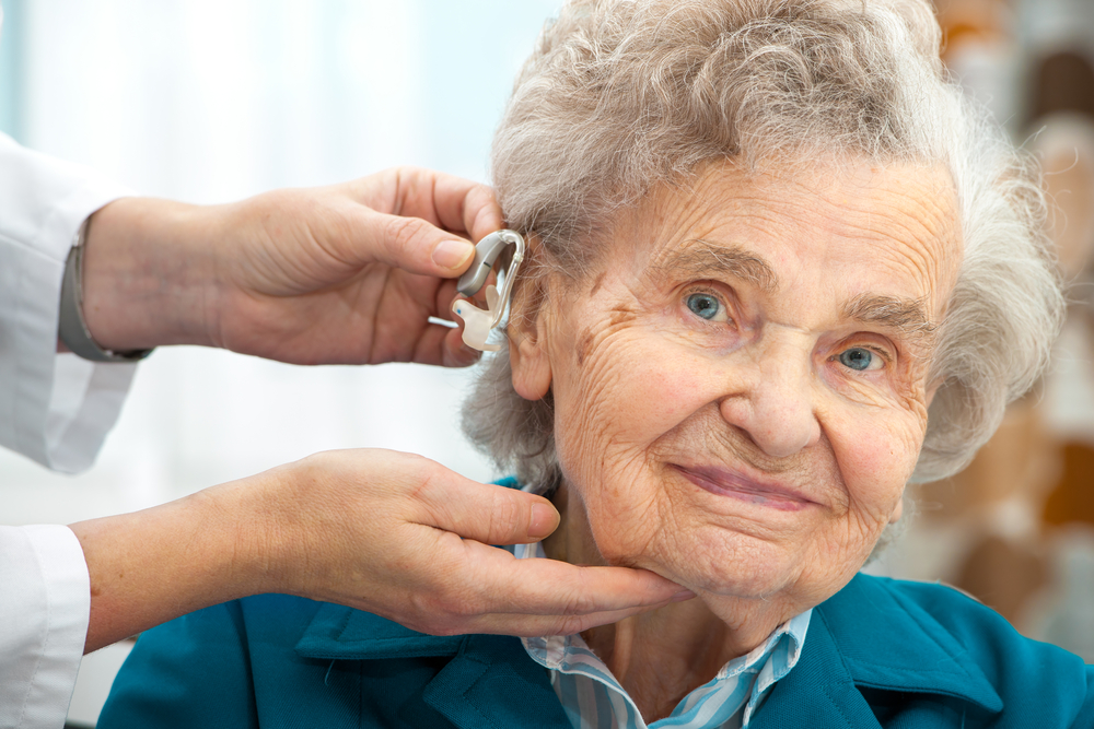 Doctor,inserting,hearing,aid,in,senior's,ear