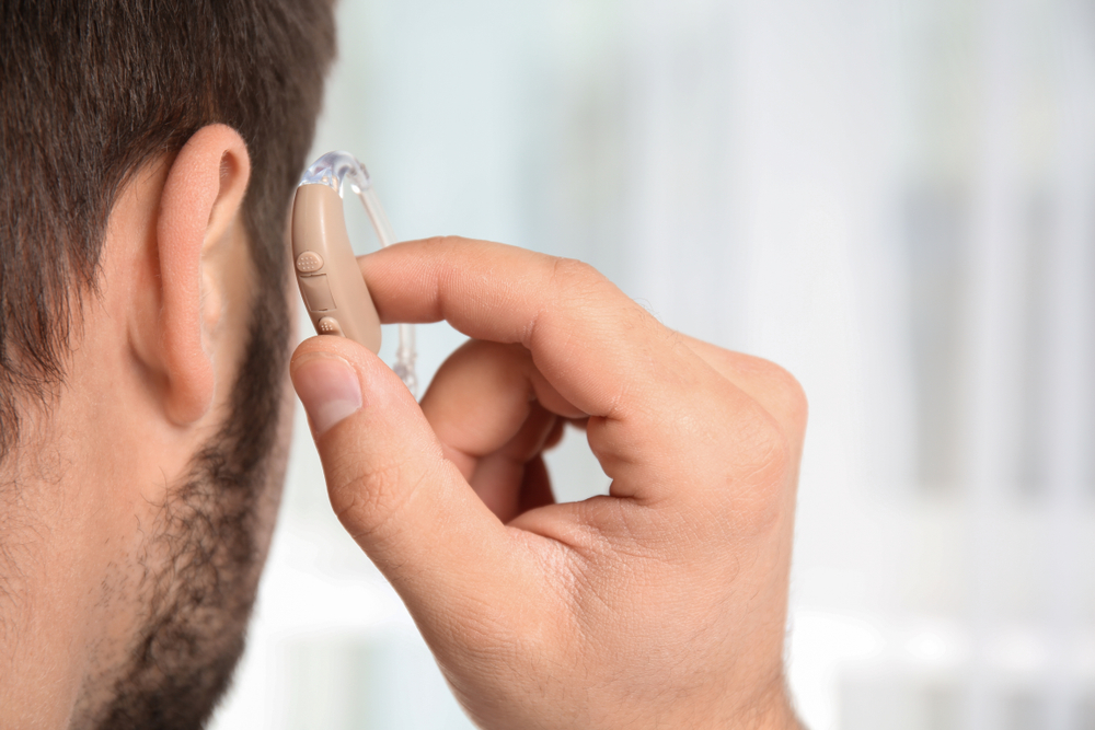 Young,man,putting,hearing,aid,in,ear,indoors